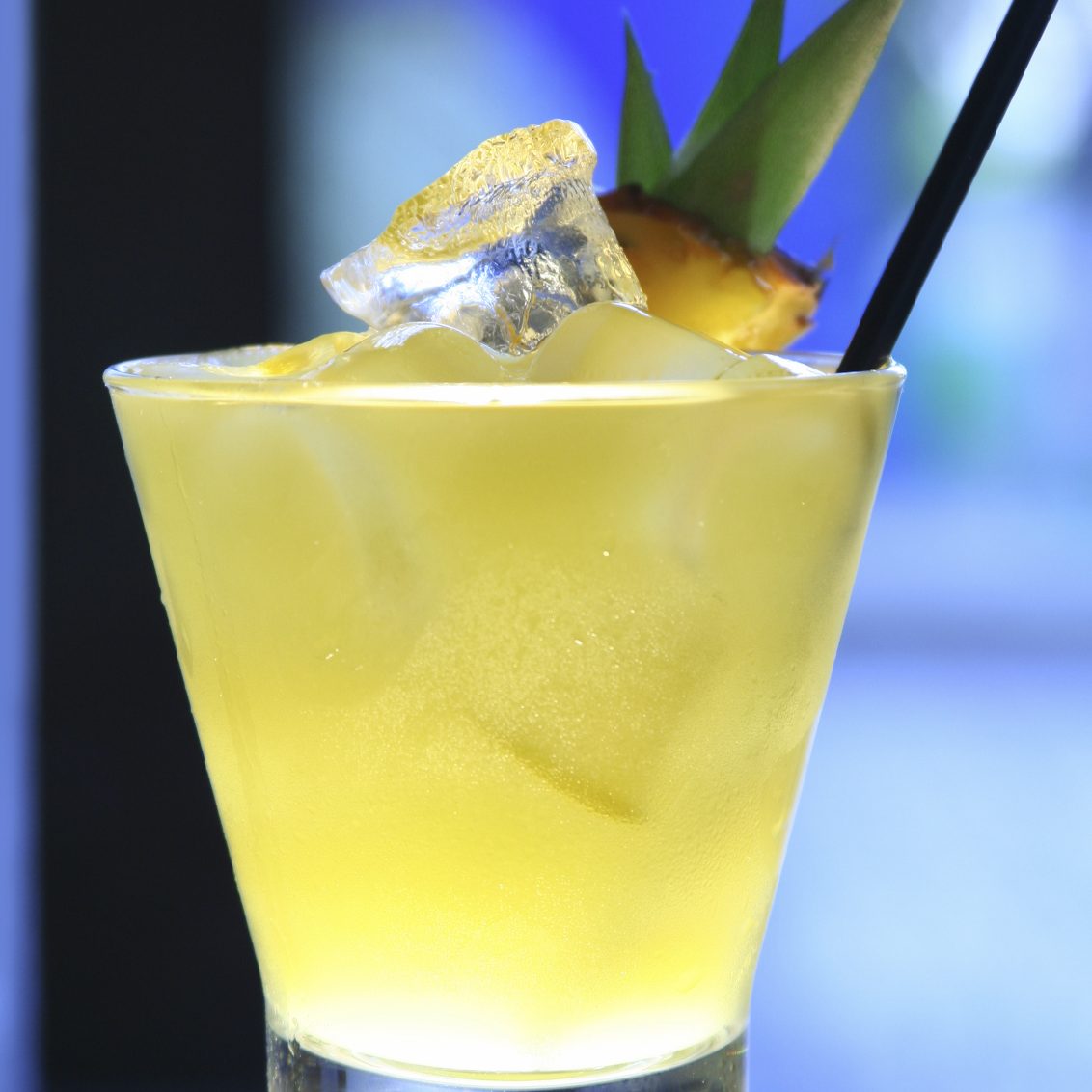 Cocktail jaune avec glaçons, garnie d'une tranche d'ananas et d'une paille.