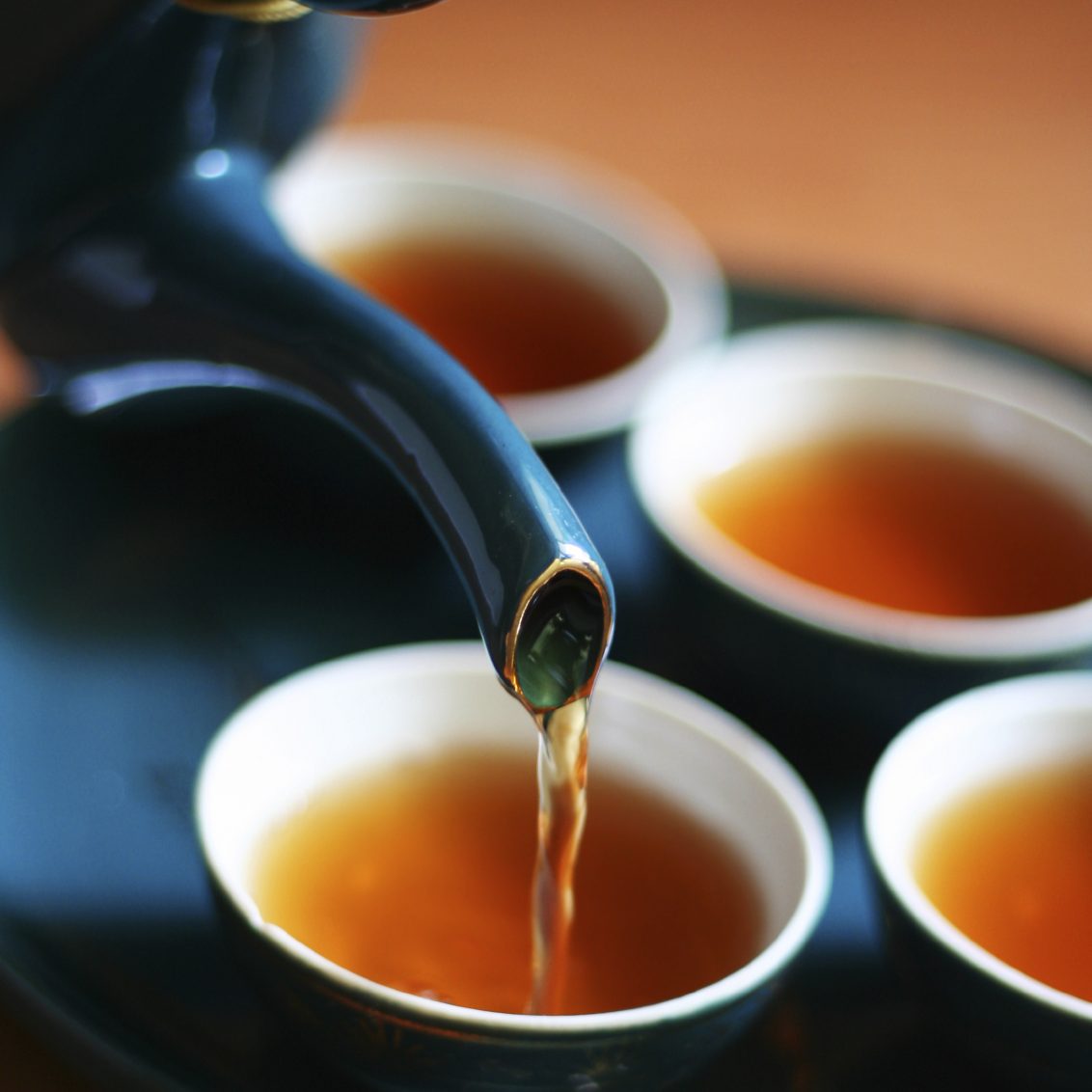 Une théière verse du thé dans des tasses blanches sur une surface en bois.